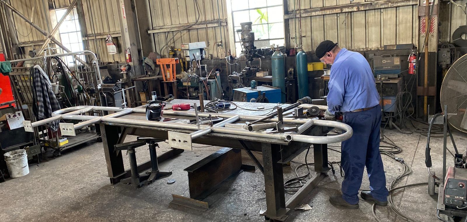 A&K fabricator welding a large steel trailer frame on the shop floor with American flag visible