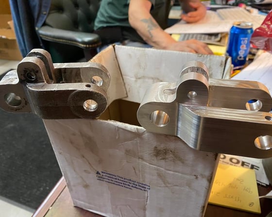 Freshly CNC-machined aluminum USPS clevis block replacement next to worn original at A&K