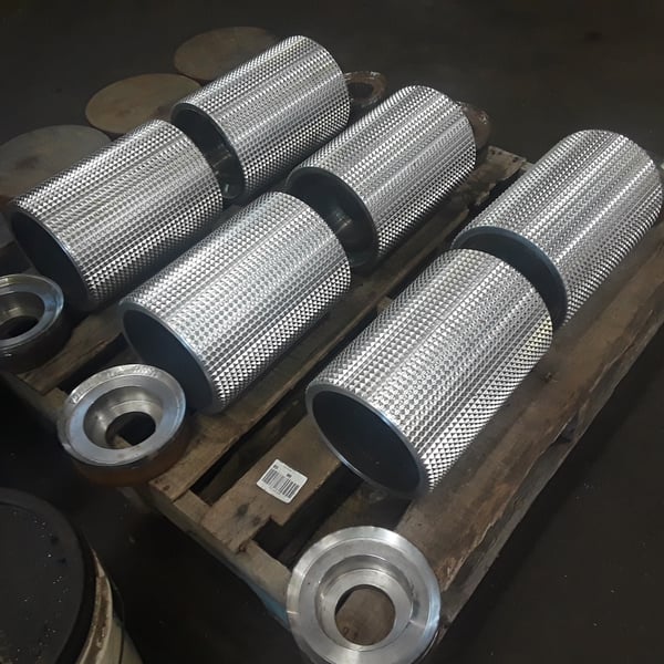 Stack of CNC-turned cylindrical steel hubs and rollers in shop