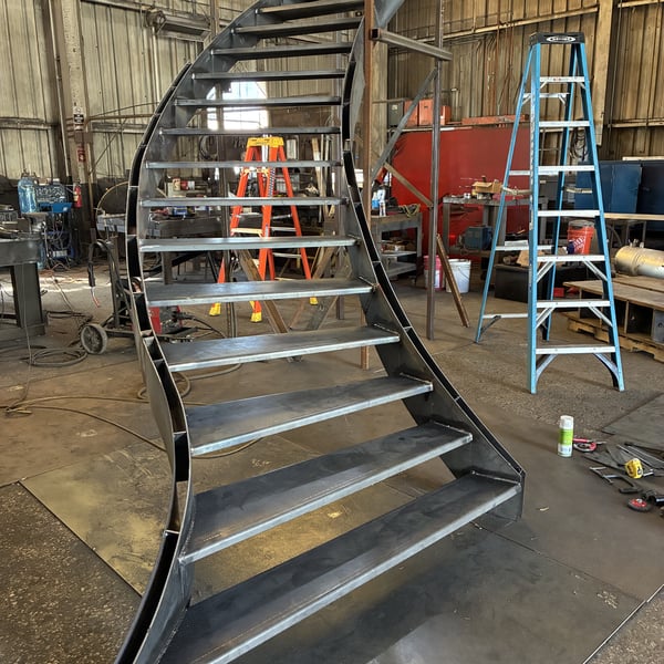 Bare-steel spiral staircase being raised during in-shop assembly