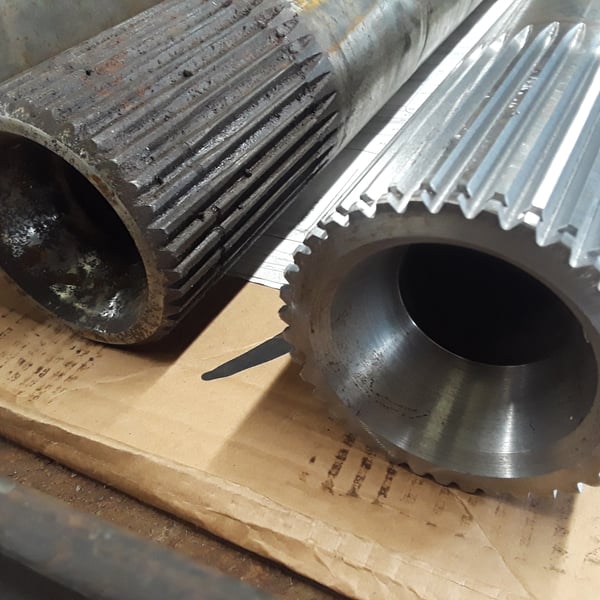 Worn splined shaft beside a freshly CNC-machined replacement showing crisp tooth detail