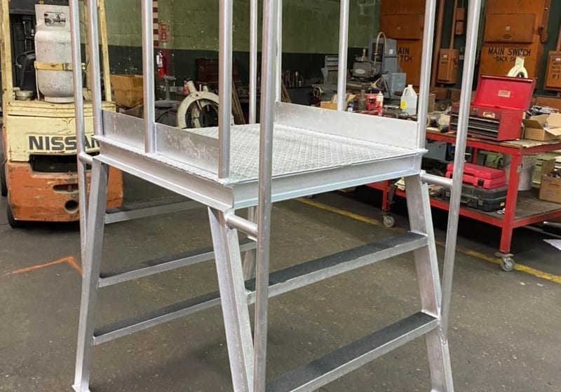 Custom aluminum conveyor walkway platform with stairs, diamond-plate deck, and safety railings fabricated by A&K