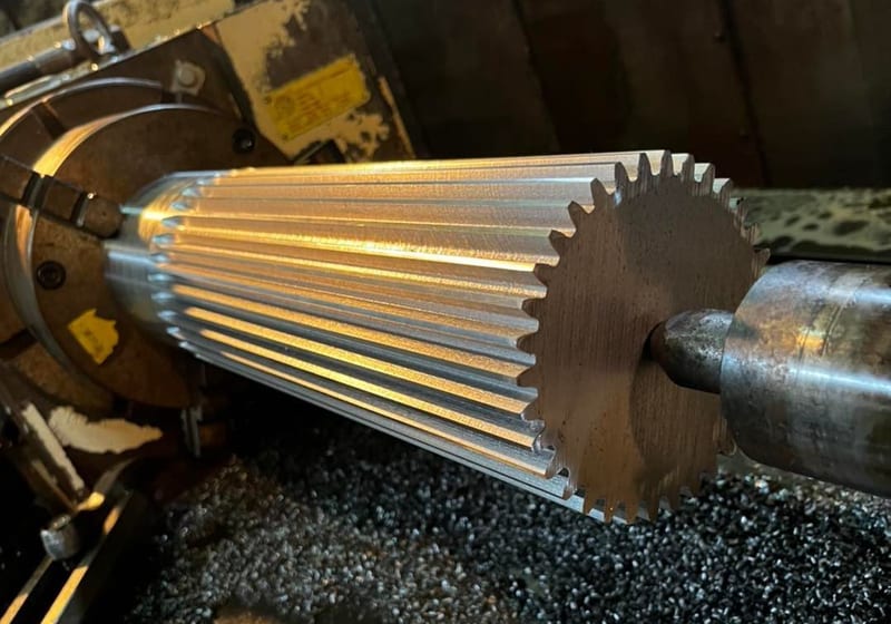 Large spur gear being machined on a lathe at A&K Machine & Fabrication — freshly cut gear teeth with metal shavings