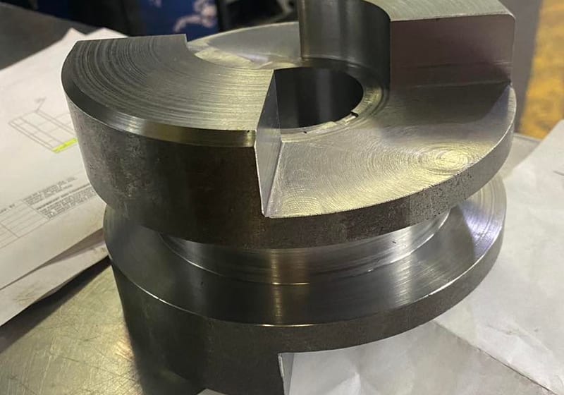 CNC-machined steel jaw coupling with keyway sitting on engineering drawings at A&K Machine & Fabrication