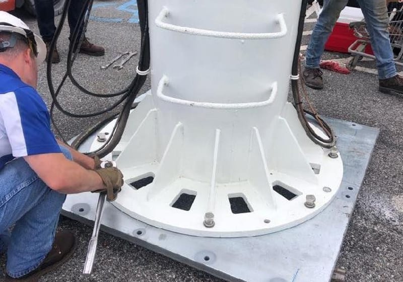 On-site installation of fabricated steel tower base plate with workers in hard hats at A&K Machine & Fabrication