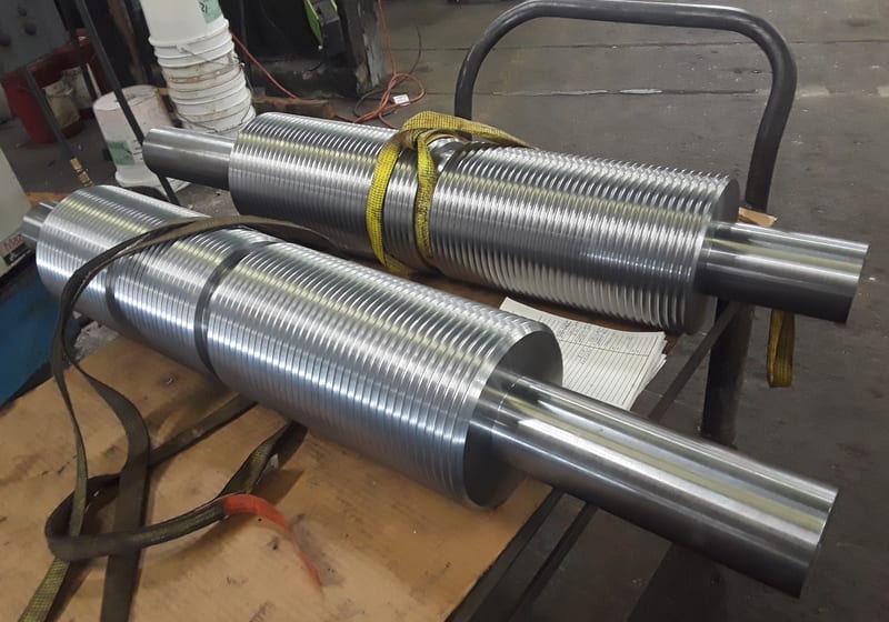 Two large CNC-machined finned conveyor idler drums strapped on a workbench, shop floor visible — A&K Machine & Fabrication, Jacksonville FL