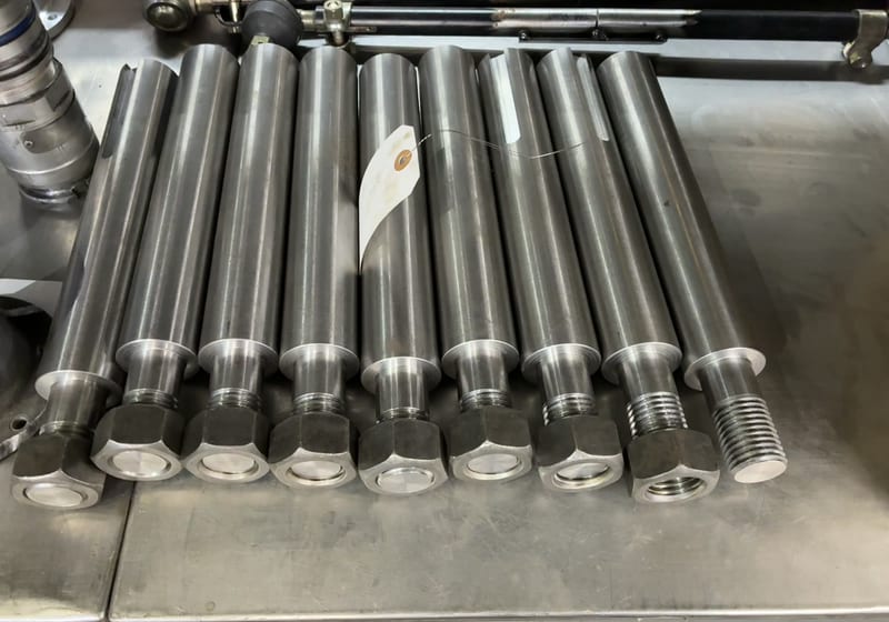 Row of ~10 long machined steel rods/shafts laid on workbench - production batch — A&K Machine & Fabrication, Jacksonville FL