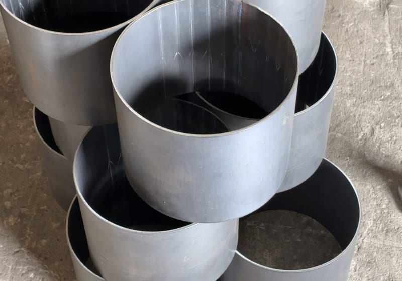 Stack of 8 large rolled steel cylinders/cans on shop floor, fresh weld seams visible — A&K Machine & Fabrication, Jacksonville FL