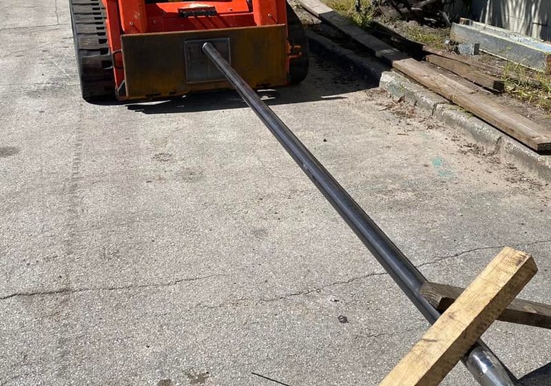 Custom steel spike attachment mounted on orange Bobcat skid steer fabricated by A&K Machine & Fabrication