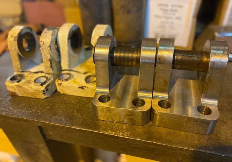 Row of machined steel clevis blocks showing worn originals vs freshly machined replacements at A&K
