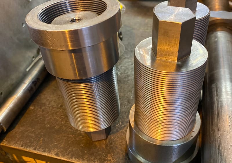 Two large custom-machined threaded steel cylinders on workbench at A&K Machine & Fabrication