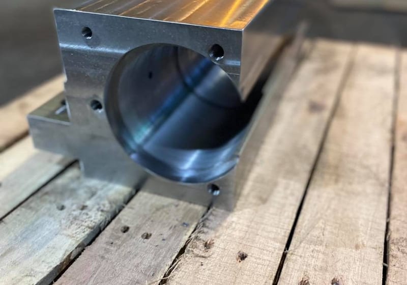 Precision CNC-machined USNR guide block with T-slot channels and cylindrical bore at A&K Machine & Fabrication